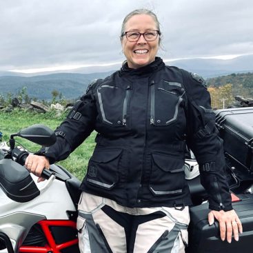 Cara Nelson, BMW Riders Trustee, leaning against her white BMW F700 GS