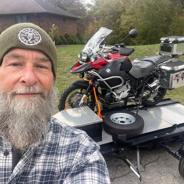 Robb Wing standing beside a open trailer with his BMW motorcycle loaded on the trailer
